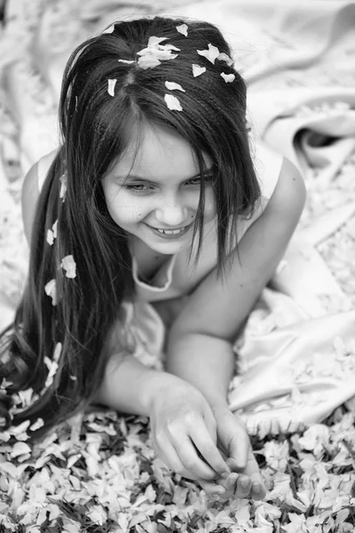 Kleines Mädchen auf grünem Gras mit Blütenblättern — Stockfoto
