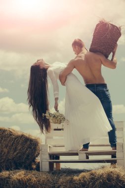 Oğlan kas gövde ile hasır sepet. Romantizm, ilişki, ilişkiler. Yaz tatil kavramı. Çiçekli beyaz elbiseli uzun saçlı kadın. Gri gökyüzü üzerinde bankta aşık çift sarılmak.