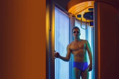 seksi sağlıklı vücut ayakta Solaryum spa salonda Mavi pantolon ve güneş gözlüğü, kaslı adam vardır güçlü kas göğüs, karın ve gövde, kopya alanı