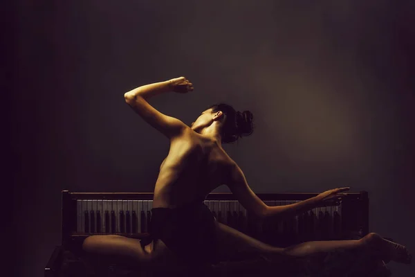 年轻女孩或妇女舞蹈家与性感灵活的芭蕾舞女演员和赤裸背部摆在旧复古木制钢琴上的灰色背景 — 图库照片