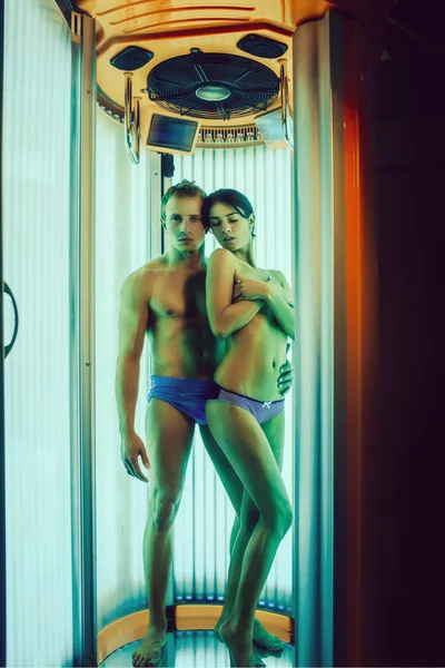 sexy couple of muscular man with healthy body and pretty naked woman or cute girl standing in solarium spa salon in pants