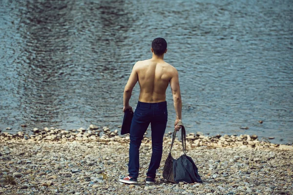 Muscular man with bag near water — Stock Photo, Image