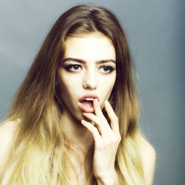 Yüz buruşturma ve el yüz ve gri arka plan üzerinde uzun sarı saçlı genç kız