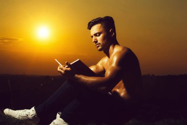 Genç yakışıklı kaslı seksi vücut ve kitap açık güneşli gün ile oturan çıplak göğüs