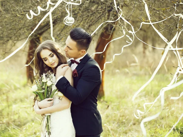 幸福的新婚夫妇合影微笑在婚礼礼服和适合用在森林里用丝带室外装饰花 — 图库照片