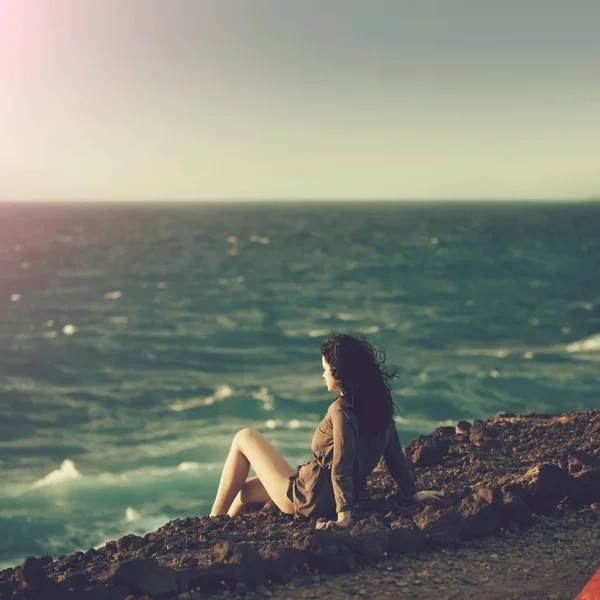 Pretty girl sitting on mountain slope above wavy sea