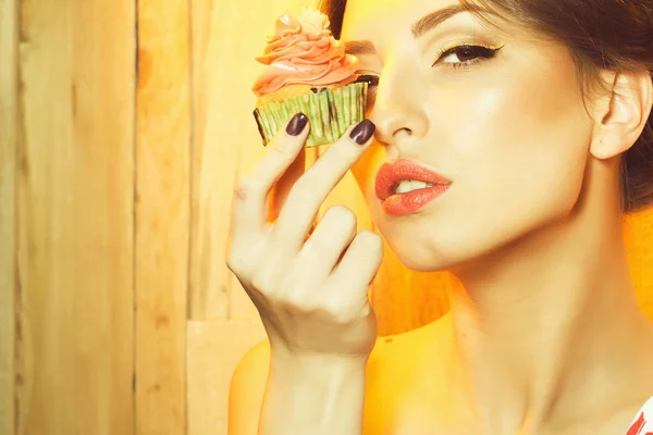 一个美丽的性感年轻女子化妆和裸露肩膀附近美味新鲜自制杯蛋糕与橙色奶油有花糖衣在绿色的纸室内 水平照片的特写视图肖像 — 图库照片