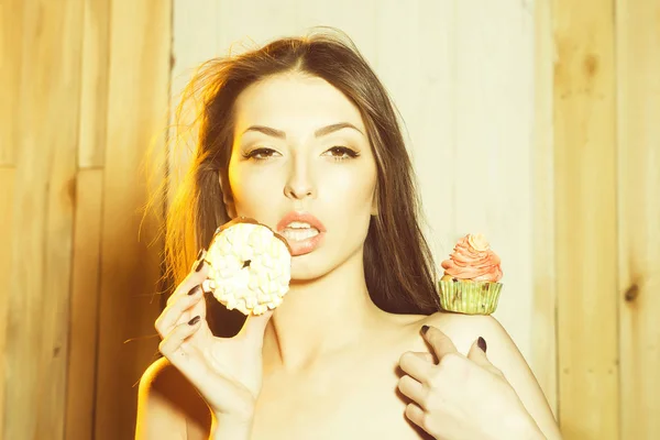 Closeup portrait of one beautiful sensual young woman with bare shoulders near tasty fresh homemade cup cake with orange cream with flower icing in green paper and doughnut  indoor, horizontal photo