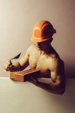 genç yakışıklı maço adam Oluşturucu ile seksi kaslı atletik güçlü vücut çıplak gövde ve güçlü karın altı paketleri ile ya da turuncu baret veya kask abs tuğla, kopya alanı tutar