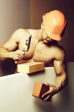 genç yakışıklı maço adam Oluşturucu ile seksi kaslı atletik güçlü vücut çıplak gövde ve güçlü karın altı paketleri ile ya da tuğla abs turuncu baret veya kask tutar