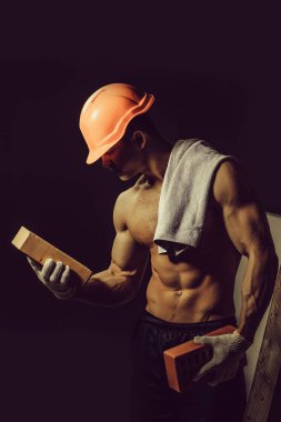 genç yakışıklı maço adam Oluşturucu ile seksi kaslı atletik güçlü vücut çıplak gövde ve güçlü karın altı paketleri ile ya da turuncu baret veya kask abs siyah arka plan üzerine tuğla tutar