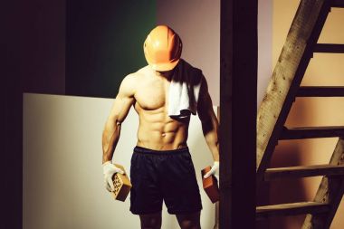 genç yakışıklı maço adam Oluşturucu ile seksi kaslı atletik güçlü vücut çıplak gövde ve güçlü karın altı paketleri ile ya da tuğla Ahşap merdiven yakınındaki abs turuncu baret veya kask tutar