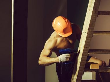 genç yakışıklı maço adam Oluşturucu ile seksi kaslı atletik güçlü vücut çıplak gövde ve güçlü karın altı paketleri ile ya da tuğla ve yumruk Ahşap merdiven yakınındaki abs turuncu baret veya kask tutar