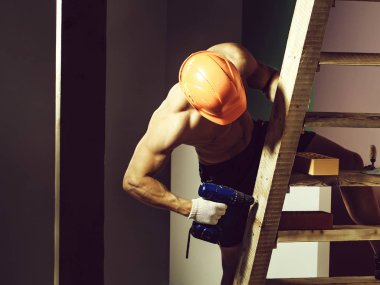 genç yakışıklı maço adam Oluşturucu ile seksi kaslı atletik güçlü vücut çıplak gövde ve güçlü karın altı paketleri ile ya da tuğla ve yumruk Ahşap merdiven yakınındaki abs turuncu baret veya kask tutar