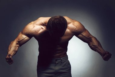 Güçlü vücut geliştirme sporcusunun seksi kaslı vücudu. Kaldırılmış elleri ve karanlık arka planda çıplak gövdesi var.