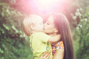 Sevimli küçük çocuk, bebeğim, evlat, öpüşme ve oldukça anne, güzel bir kadın, sarılma yeşille, park güneşli açık havada doğal zemin üzerine yaz