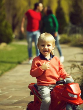 Yüz ve plastik oyuncak Bisiklet Park el ele tutuşarak ailesiyle oturan sarışın gülümseyen mutlu küçük çocuk arka plan bulanık
