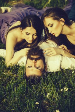 Yakışıklı yeşil çim güneşli açık mor elbise iki genç güzel kadınlarla yalan Beyaz gömlekli sakallı