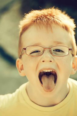 Komik küçük çocuk gözlük Kızıl saçlı dilini açık havada güneşli yaz gününde koyar