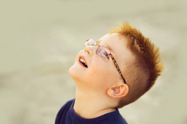 Gri zemin üzerine yaz gününde mutlu bebek oğlan mavi tişört ve gözlük Kızıl saçlı örnek alıyor