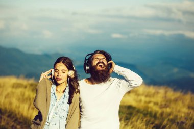 Battaniyeye sarılı genç bir çift güzel kız ve sakallı hippi sakallı bir adam dağ sahnesinde kulaklıkla müzik dinliyor.