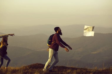 Sakallı adam hipster ve güzel kızlar seyahat etmek harita üzerinde dağın tepesinde sisli gökyüzü Rüzgar gibi geçti yakalamak