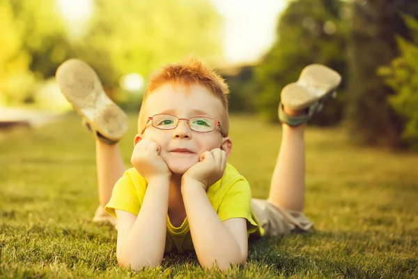 Sarı gömlek ve sevimli yüzü yeşil çimenlerin üzerinde yaz günü doğal zemin üzerine açık döşeme gözlük Kızıl saçlı erkek mutlu bebek
