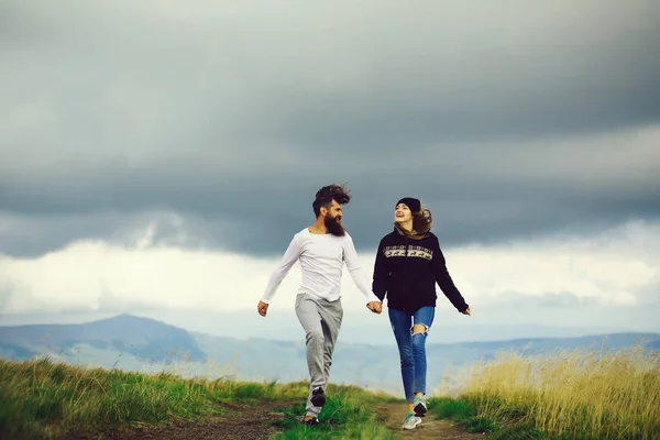 Couple of handsome bearded man in white shirt and pretty young cute girl or woman in black hoody holding hands and bouncing on cloudy sky background