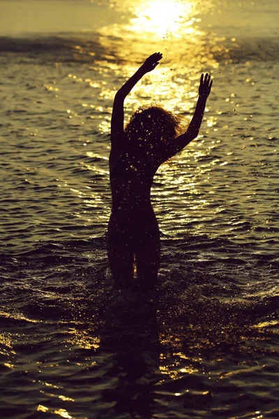 young woman silhouette on beach swimming in sea or ocean water in evening or twilight sunset summer day on natural background