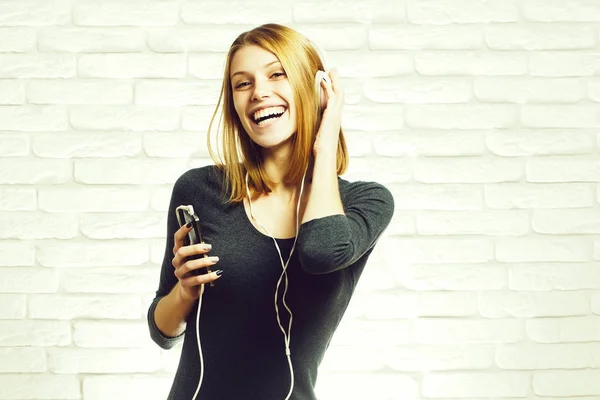 れんが造りの白い背景にスマート フォンにイヤホンで音楽聴いて幸せなきれいな女の子や赤い髪のかわいい美人女性モデル — ストック写真