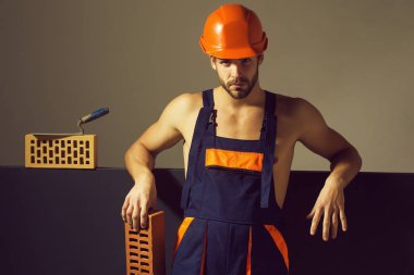 genç yakışıklı sakallı maço adam Oluşturucu seksi kaslı atletik güçlü vücut ile mavi üniforma ve turuncu baret veya kask tuğla ve spatula yakınındaki güçlü elinde vardır