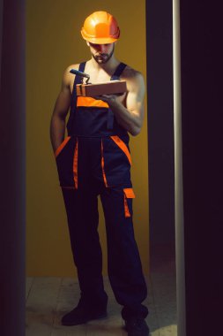 genç yakışıklı maço adam Oluşturucu ile seksi atletik güçlü vücut mavi üniforma güçlü elleri ve tuğla ve spatula turuncu baret veya kask tutar kas sakallı