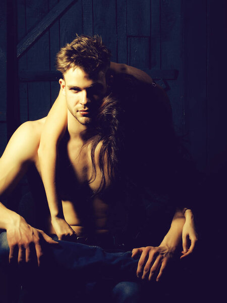 Молодая чувственная пара сексуальных мускулистых мачо мужчина с голым туловищем и довольно топлесс женщина обнимает любовника в помещении на деревянном фоне, вертикальная картина
