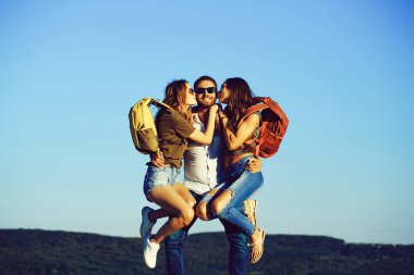 Sakallı yakışıklı adam iki sarışın çok seksi sevimli kız ya da kadın kot pantolon ve şort sırt çantaları ile açık güneşli mavi gökyüzü arka plan üzerinde tutar