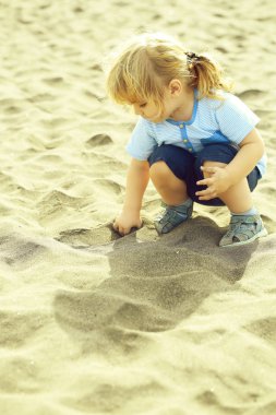 Şirin bebek çocuk sarı saçları at kuyruğu mavi tshirt ve şort ile doğal kum kumlu plaj açık havada üzerinde ile güneşli, yaz günü gri dokulu arka plan çalış