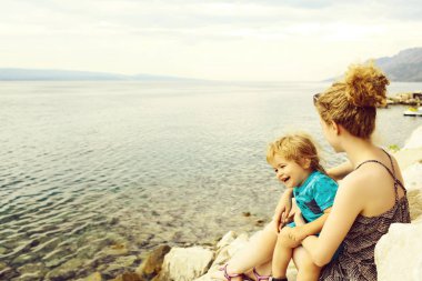 Mutlu anne ve bebek evlat taşlar mavi deniz plajda oturmak ve yaz günü güzel zevk