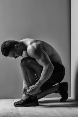 genç yakışıklı maço adam vücut geliştirmeci kısa filmlerde çıplak gövde ile seksi kaslı atletik güçlü gövdeli spor ayakkabıları Studio Sarı zemin üzerine bağcıklarımı bağlar