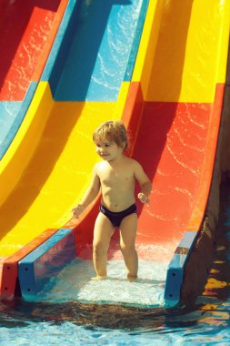 Sarışın saçlı mutlu sevimli bebek çocuk kaydırağı su veya aqua park açık renkli arka plan üzerinde gün güneşli yaz rides