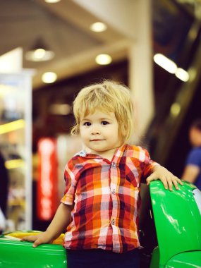 Şirin bebek çocuk sarışın çocuk Kareli gömlekli yeşil oyuncak araba eğlence parkında kullanıyor.