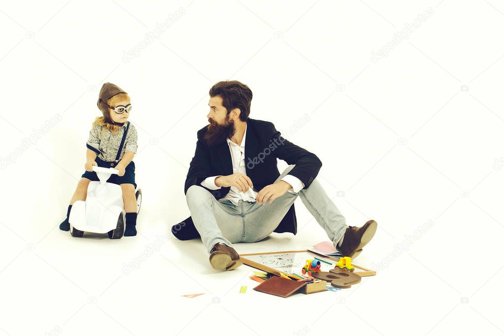 small boy kid driver or pilot sitting on plastic toy cat in stylish shirt with bearded man father with beard near school appliances of blackboard letter pen and paper isolated on white background