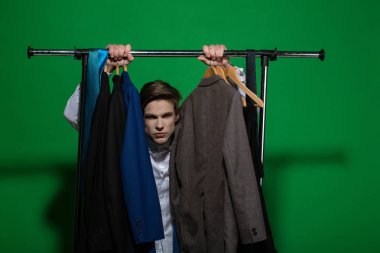 Adam dolap askı raf ceketler ile tutun. İş moda, stil kavramı. Alışveriş, satış, satınalma. Yeşil zemin üzerine beyaz gömlekli bir iş adamı. Giyim, Soyunma Dolabı.