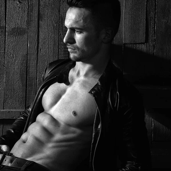 Seksi şehvetli kas şık yakışıklı genç çıplak gövde oturan ahşap arka plan üzerinde dikey resim kapalı deri ceketli