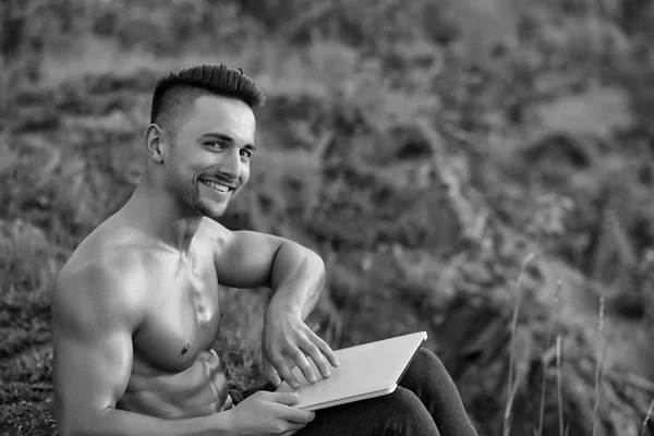 Uomo muscoloso sorridente con computer portatile all'aperto — Foto Stock