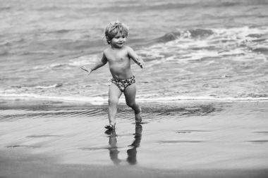 Doğal zemin üzerine dalgalar ile deniz ya da okyanus su ıslak kum plajı üzerinde şirin neşeli bebek çocuk sarı saçları at kuyruğu şort ile çalışır