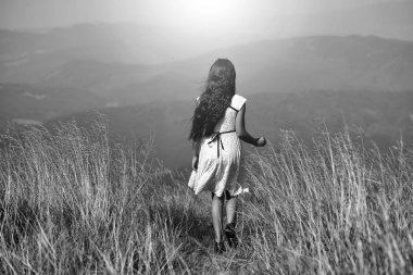 Beyaz dantel yaz aylarında genç küçük esmer kızın arka viev elbise dağ vadide derin kuru spikelet çim ile bahar güneşli bir günde açık doğal mavi arka plan üzerinde yatay resim yürüyüş