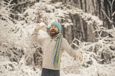 Kar mücadele, spor, dinlenme. Sakallı adam gülümseme ile karlı ormandaki kartopu. Isı, soğuk, soğuk dalgası. Cilt Bakımı, sakal Bakımı kış. Hipster termal ceket, şapka, eşarp, sakal sıcak kış içinde