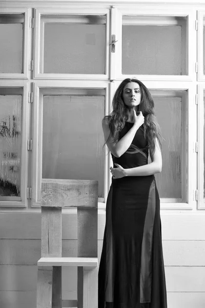 漂亮的女孩或美丽时尚女人与长长的金发 穿着黑色礼服站在白色的木椅上迷离的窗口背景 — 图库照片