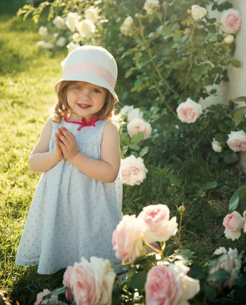 孩子微笑着盛开的玫瑰花在绿草上 女孩在帽子与祈祷的手在夏季花园 未来和繁荣 纯洁和青春的概念 发芽与生长 — 图库照片