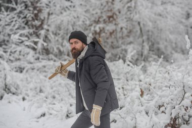 Sakallı adam karlı ormanda balta ile. Isı, soğuk, soğuk dalgası, kar yağışı. Kışın, sakal sıcak kış aylarında Cilt Bakımı ve sakal bakımı. Kamp, seyahat ve kış dinlenme. Adam oduncu balta ile.