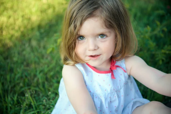 阳光明媚的夏日 可爱的脸庞上长着棕色眼睛的小女孩坐在绿草上 天真和青年概念 休闲和乐趣 — 图库照片